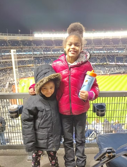 Two children smiling from stadium seats during a night baseball game
